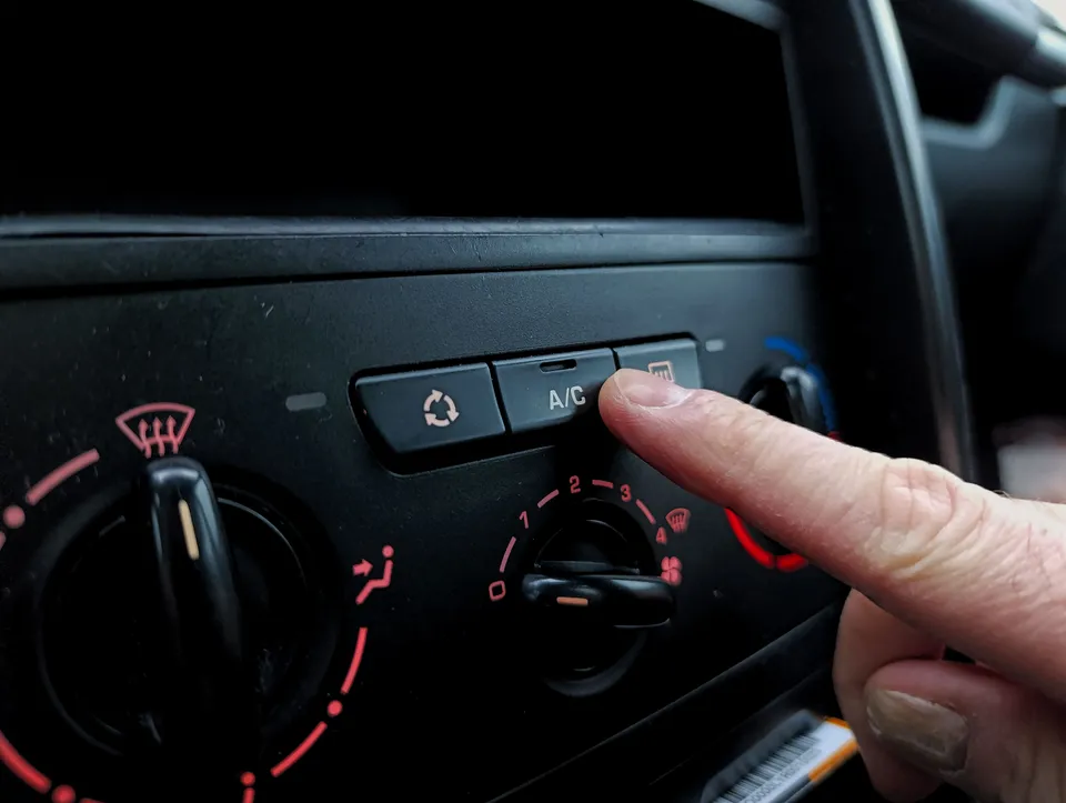 Finger pressing the A/C button on a car dashboard climate control panel